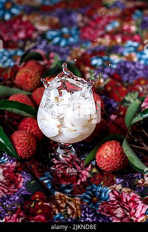 A vertical closeup of glass with litchi juice on the colorful tablecloth. Selected focus. Stock Photo