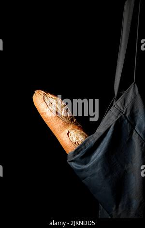 A vertical shot of tasty just baked baguette in a reusable cloth bag isolated on a black background Banque D'Images