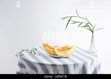 A still life photo of melon slices on a round table and bamboo leaves in a vase Stock Photo