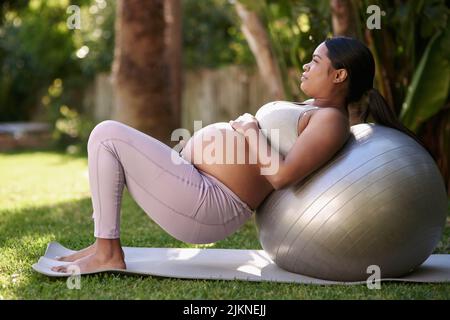 Une femme enceinte qui fait de l'exercice avec une balle de stabilité à l'extérieur. Banque D'Images