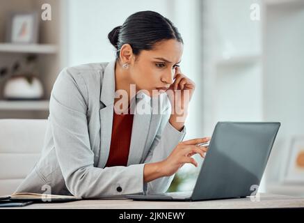 Femme d'affaires sérieuse, concentrée et africaine lisant un e-mail, naviguant en ligne ou recherchant des idées sur un ordinateur portable seul dans un bureau au travail. Un Banque D'Images
