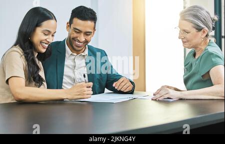 Signature de leur plan d'investissement. Un jeune couple passe en charge de la paperasserie lors d'une réunion avec son conseiller financier. Banque D'Images