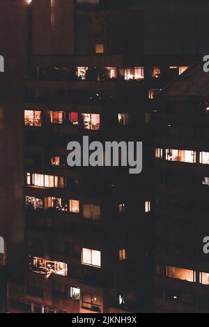 Une photo verticale d'un bâtiment la nuit avec plusieurs fenêtres éclairées Banque D'Images