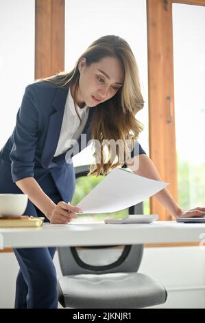 Portrait, magnifique et professionnelle jeune femme d'affaires asiatique ou directrice générale qui examine le rapport financier à son bureau. Banque D'Images