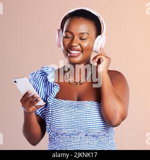 La créativité prospère dans la solitude. Photo en studio d'une jeune femme utilisant un smartphone et un casque sur fond rose. Banque D'Images