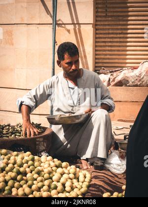 Une belle photo d'un vendeur de rue portant le galabeya assis sur le sol vendant le citron et l'okra dans un marché local un jour ensoleillé à Assouan, en Égypte Banque D'Images