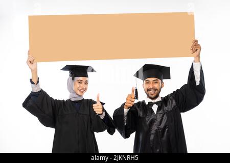 Couple d'étudiants diplômés portant tosa tenant un espace vide en carton Banque D'Images