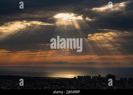 A scenic view of sun rays passing through dark clouds over a coastal town Stock Photo