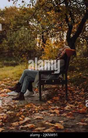 Jeune couple assis sur un banc et regardant vers le haut en saison d'automne Banque D'Images