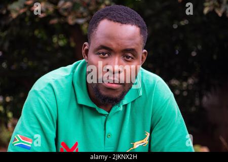Un homme noir adulte assis dans un t-shirt vert avec drapeau du zimbabwe regardant la caméra Banque D'Images