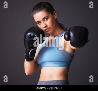 Shes plus féroces que vous ne le pensez. Portrait d'une jeune femme portant des gants de boxe sur un fond gris. Banque D'Images