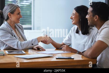 Notre maison de verre jettera des pierres à tout ce qu'il passe. Un jeune couple partageant une poignée de main avec un conseiller theyre réunion pour discuter de la paperasserie d'un bureau. Banque D'Images