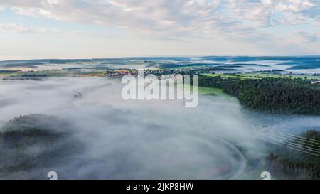 A fog on top of a village surrounded with greenery Stock Photo