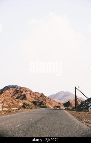 A vertical shot of a long empty road stretching through an area full of sandy hills during daytime Stock Photo