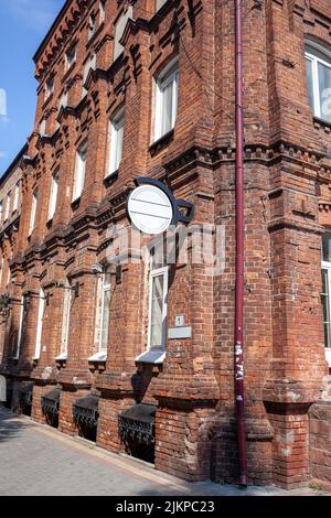 Un vieux grand bâtiment en briques avec un panneau blanc pour le nom d'un café ou d'un magasin. Bâtiment en brique dans le centre de la ville mais contre le ciel bleu. Banque D'Images