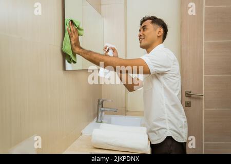 un concierge asiatique de sexe masculin vaporise et essuye le miroir avec un chiffon Banque D'Images