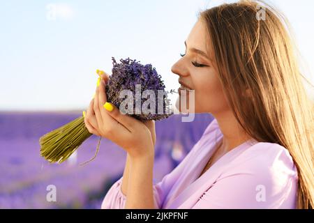 Jeune femme en robe tenant un bouquet de fleurs debout dans le champ de lavande Banque D'Images