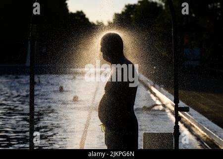 Hanovre, Allemagne. 03rd août 2022. Un homme prend une douche tôt le matin dans la piscine extérieure d'Annabad à la lumière du soleil levant. Credit: Julian Stratenschulte/dpa/Alay Live News Banque D'Images