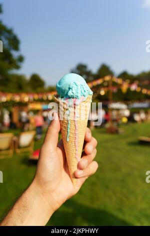 Cône de crème glacée à la main. Dessert sucré sur pique-nique d'été arrière-plan flou. Concept de la nourriture, de l'été, de la crème glacée. Mise au point sélectionnée. Photo de haute qualité Banque D'Images