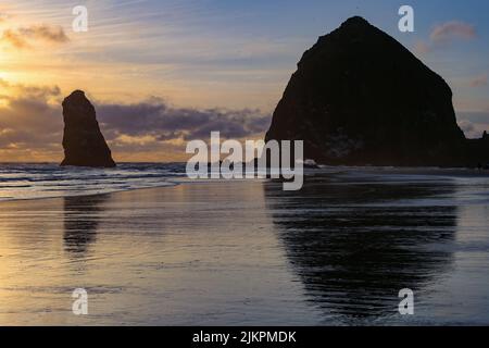 A silhouette of the Haystack Rock in Cannon Beach reflecting on the water surface at sunrise, Oregon, United States Banque D'Images