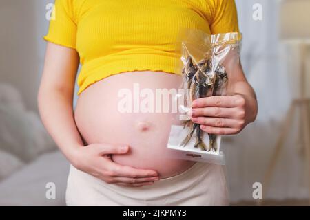 Poisson séché dans les mains d'une femme enceinte, salon à la maison Banque D'Images