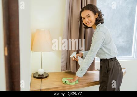 femme de ménage souriant en vaporisant et en essuyant la table Banque D'Images