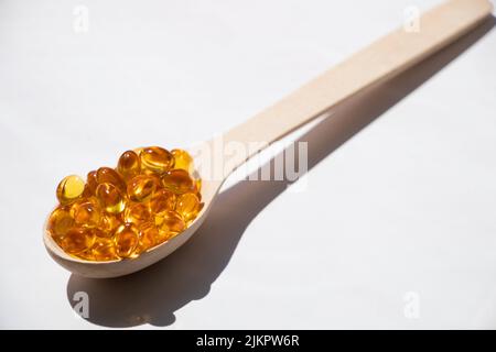 Les pilules d'huile de poisson se trouvent dans une cuillère en bois sur un fond isolé, vitamines et suppléments, santé Banque D'Images