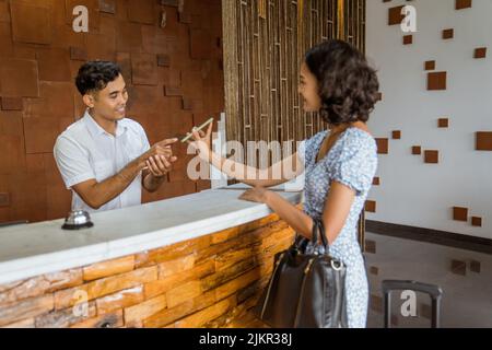 Une cliente montrant l'écran d'un smartphone à la réceptionniste dans le hall de l'hôtel Banque D'Images
