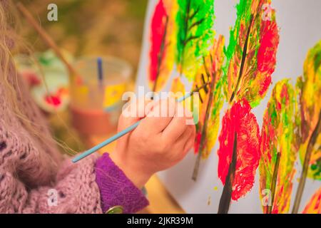 petite fille artiste avec un pinceau et des peintures dans ses mains en automne dans le parc dessine un paysage avec des feuilles sur toile Banque D'Images