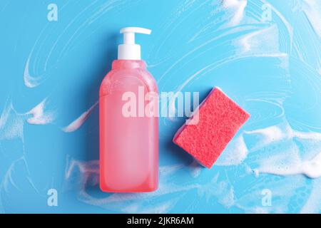 Liquide vaisselle et éponge rouge sur fond bleu moussant. Concept de nettoyage. Banque D'Images