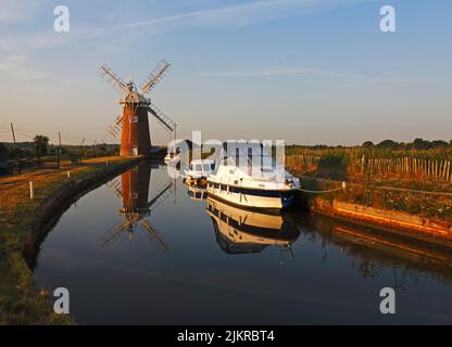 Vue sur la digue et le moulin à vent avec des bateaux réfléchis et amarrés sur les Norfolk Broads à Horsey, Norfolk, Angleterre, Royaume-Uni. Banque D'Images