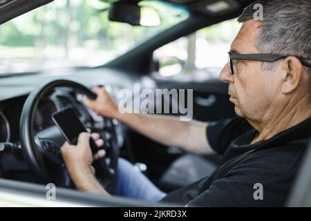 Senior actif dans sa 70s conduite d'une voiture et usig son téléphone mobile Banque D'Images