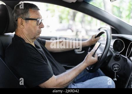 Senior actif dans sa 70s conduite d'une voiture et usig son téléphone mobile Banque D'Images