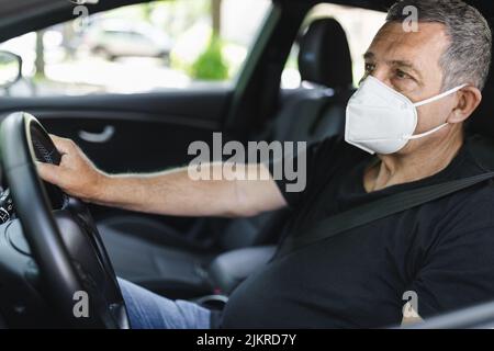 Senior dans sa 70s conduite d'une voiture portant un masque facial pour la protection contre le virus corona Banque D'Images