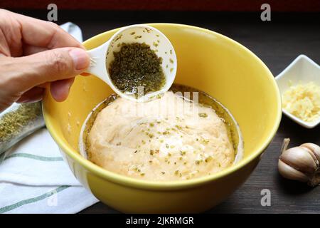Versez à la main de l'huile d'olive avec des herbes sur de la pâte à pétrir pour cuire du pain italien Focaccia Banque D'Images