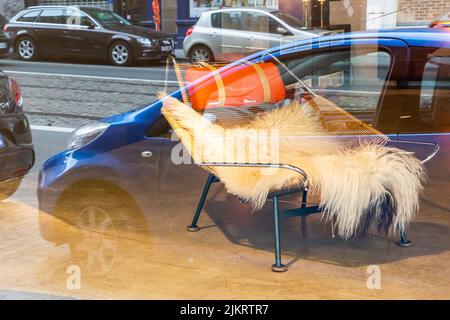 Se reflète dans une fenêtre de magasin: Voitures garées et un fauteuil à vendre, couvert de peau d'animal. Banque D'Images