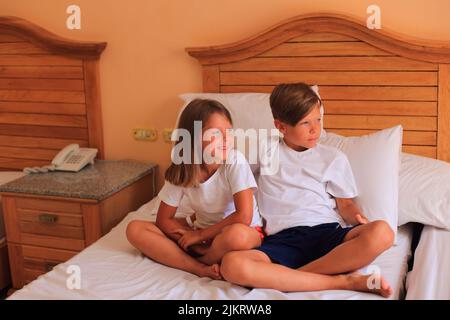 En vacances, deux enfants s'étendent sur un lit avec des draps blancs dans une chambre d'hôtel. Les enfants jouent sur le lit avec des draps blancs à la maison. Garçon et fille avant d'aller au lit à la maison Banque D'Images