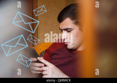 Un jeune homme aux cheveux bruns, un européen, est assis au téléphone et lit les nouvelles en ligne attentivement. Des taches de rousseur et une mole sur le visage. Veste rouge. Front flou Banque D'Images