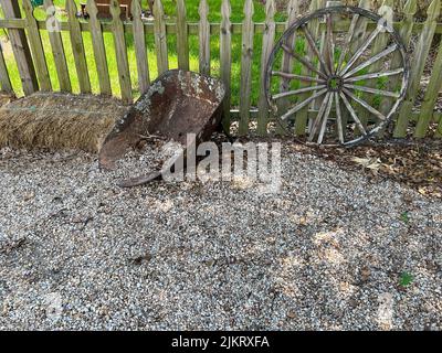 Une roue rustique de brouette et de chariot, adochée à une clôture en bois sur une ferme. Banque D'Images