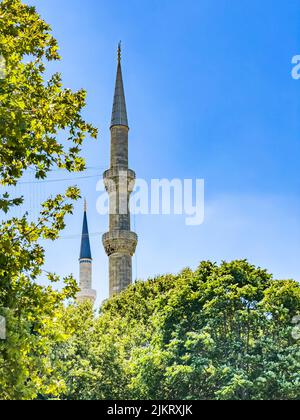 Vue partielle d'en dessous sur deux minarets de la mosquée à l'architecture islamique et arbres verts contre le ciel bleu à Istanbul, Turquie. Arrière-plan vertical Banque D'Images