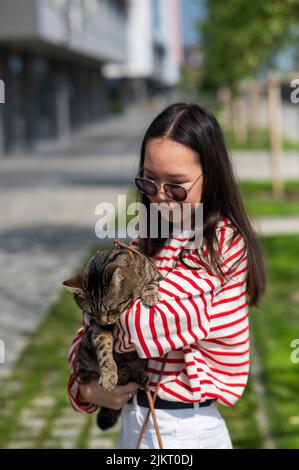 Jeune femme tenant le chat tabby dans ses bras à l'extérieur. Banque D'Images