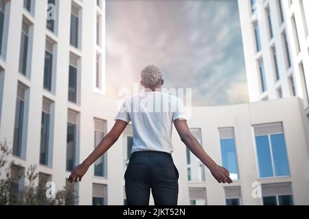 Vue arrière d'un homme anonyme aux cheveux teints dans des vêtements décontractés debout avec bras écartés contre des bâtiments modernes de plusieurs étages dans la ville Banque D'Images