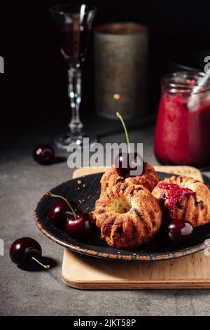 Petits gâteaux avec cerises sur fond sombre. Banque D'Images