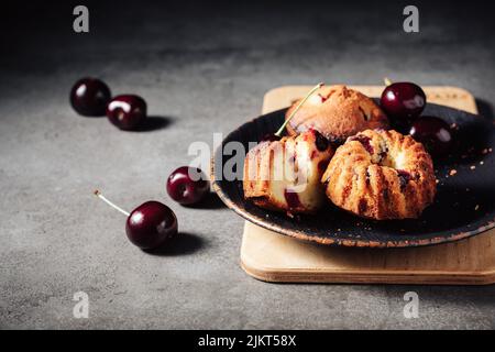 Petits gâteaux avec cerises sur fond sombre. Banque D'Images