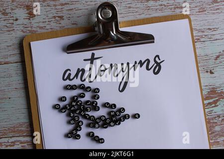 Vue de dessus du presse-papiers en papier avec des antonymes de texte et des perles d'alphabet. Banque D'Images