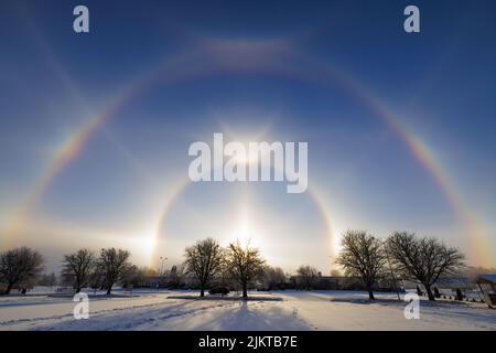 A scenic view of a double rainbow in a park covered with snow on a winter day Stock Photo