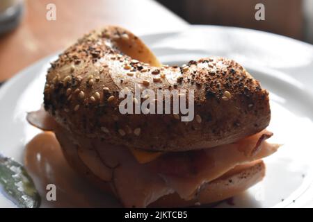 A half bagel stuffed with ham and cheese placed on a white plate Stock Photo