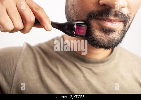Homme indien sur fond blanc utilisant le microneedling pour la croissance de la barbe. Banque D'Images