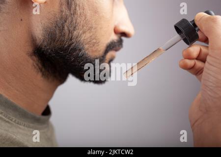 un beau gars qui montre un compte-gouttes rempli d'huile de barbe et qui va l'appliquer pour la pousse de la barbe sur un fond de couleur unique Banque D'Images