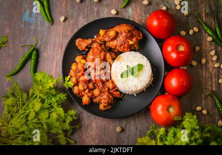 Une vue de dessus de poulet cubain fricassée de riz sur une assiette noire décorée de légumes verts et de tomates Banque D'Images